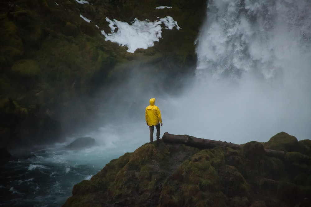 personne en manteau jaune debout près des chutes d’eau pendant la journée