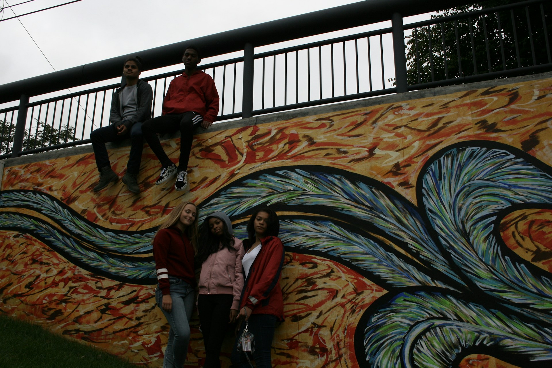 A group of young artists painting the mural together under a sunny sky, surrounded by lush tropical plants.