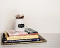 A stack of children's books is neatly arranged on a white surface. On top of the stack is a white jar labeled 'READ' filled with twig-like colored pencils. The books include titles like Hop on Pop by Dr. Seuss, Pinocchio, and Beauty and the Beast.