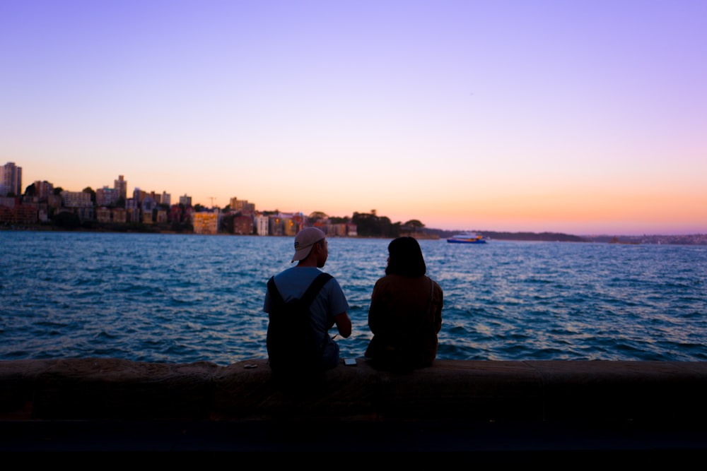 man and woman sitting facing body of water