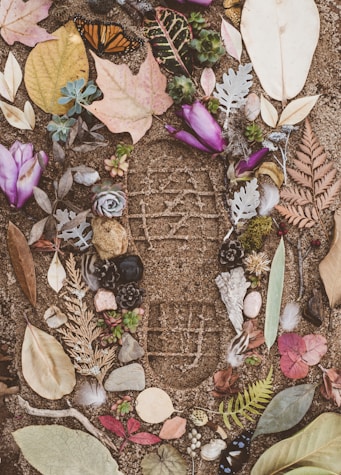 assorted flowers and leaves on sand with shoe mark