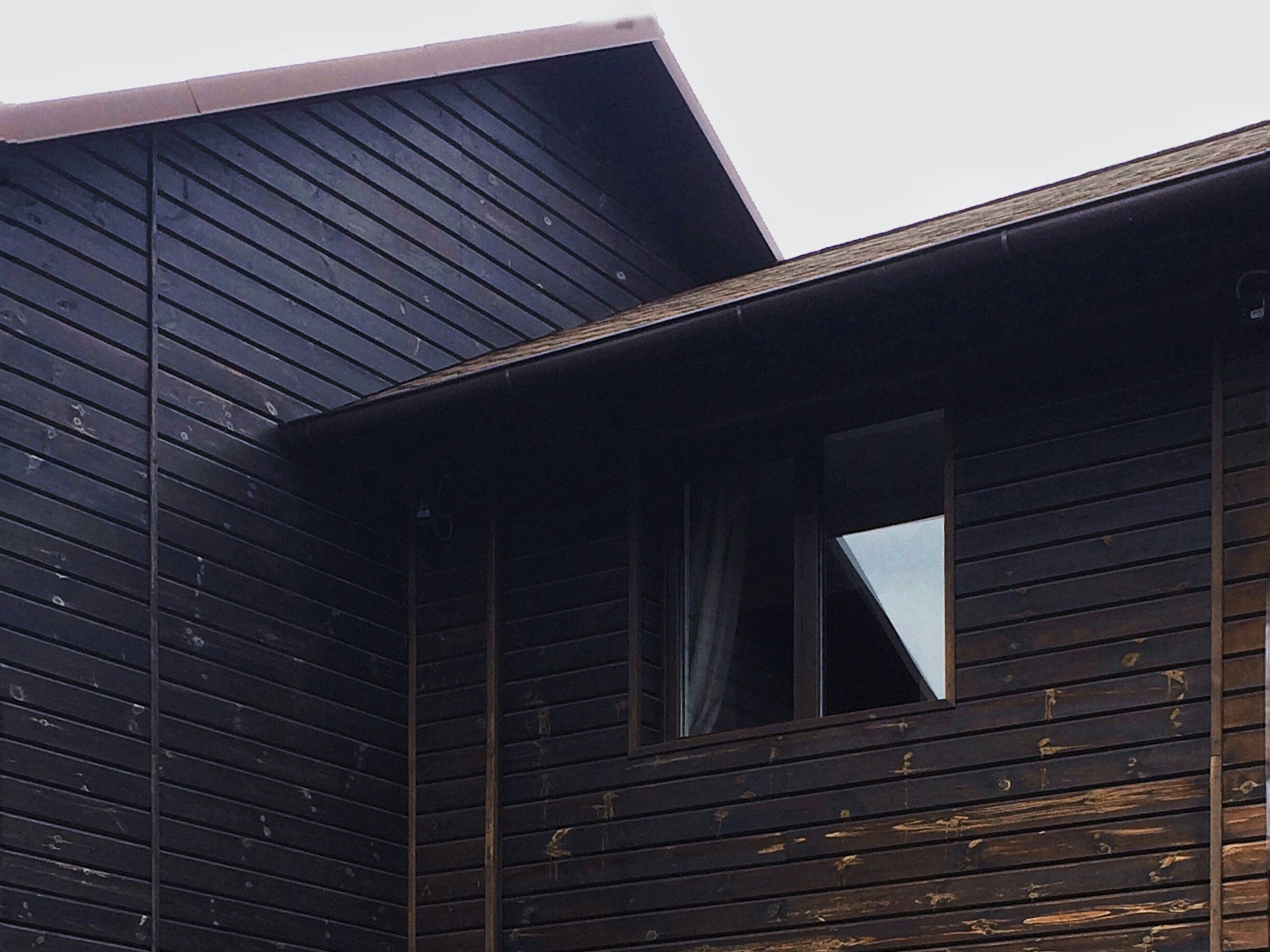 Custom home exterior with board-and-batten siding, stone foundation, tall fir trees, dramatic overcast sky, deep shadows
