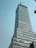 A tall, modern skyscraper with numerous glass windows and a slightly angular structure. A banner hangs near the lower section.