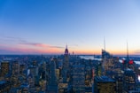 A panoramic cityscape with modern buildings lit up at dusk.