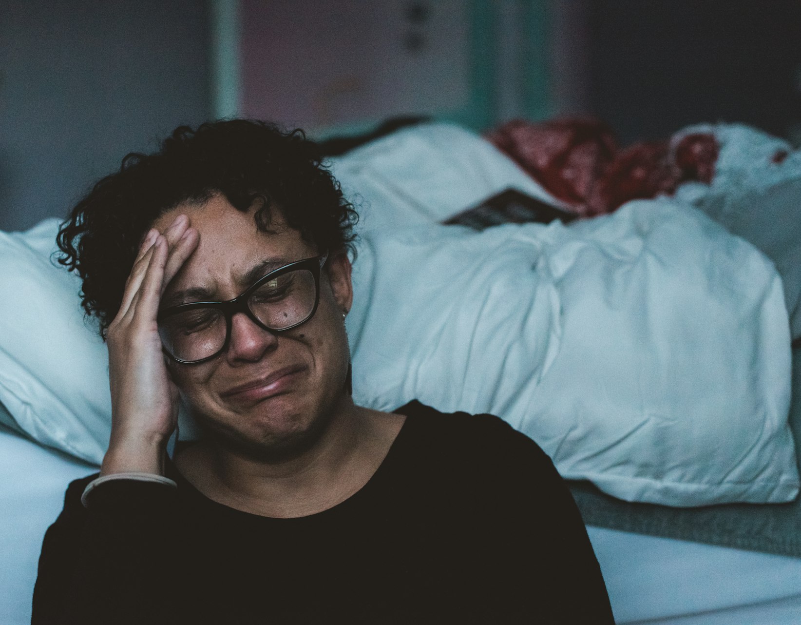 Woman with glasses sitting beside a bed with her head in her hand, crying. When you feel like giving up, read this Inspired Idiots blog post.