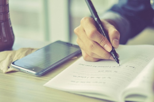 a person writing on a piece of paper with a pen
