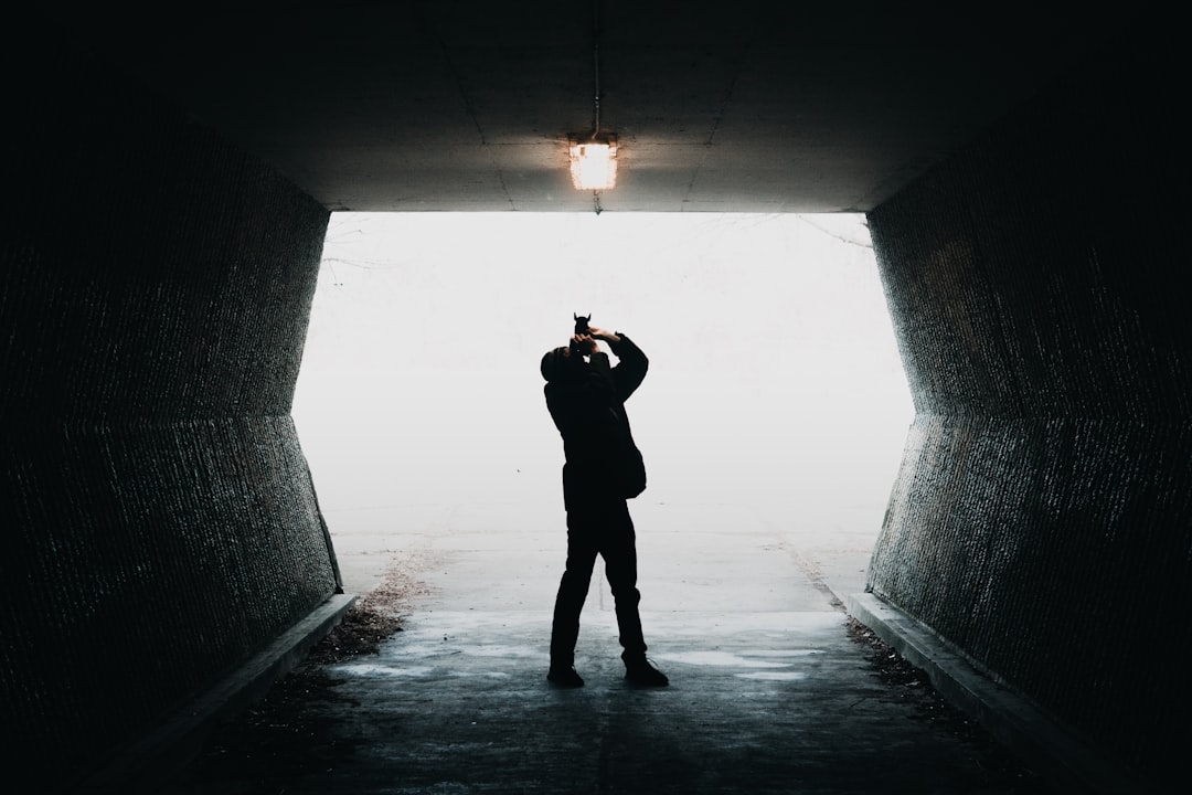 silhouette of man taking photo of light inside tunnel way