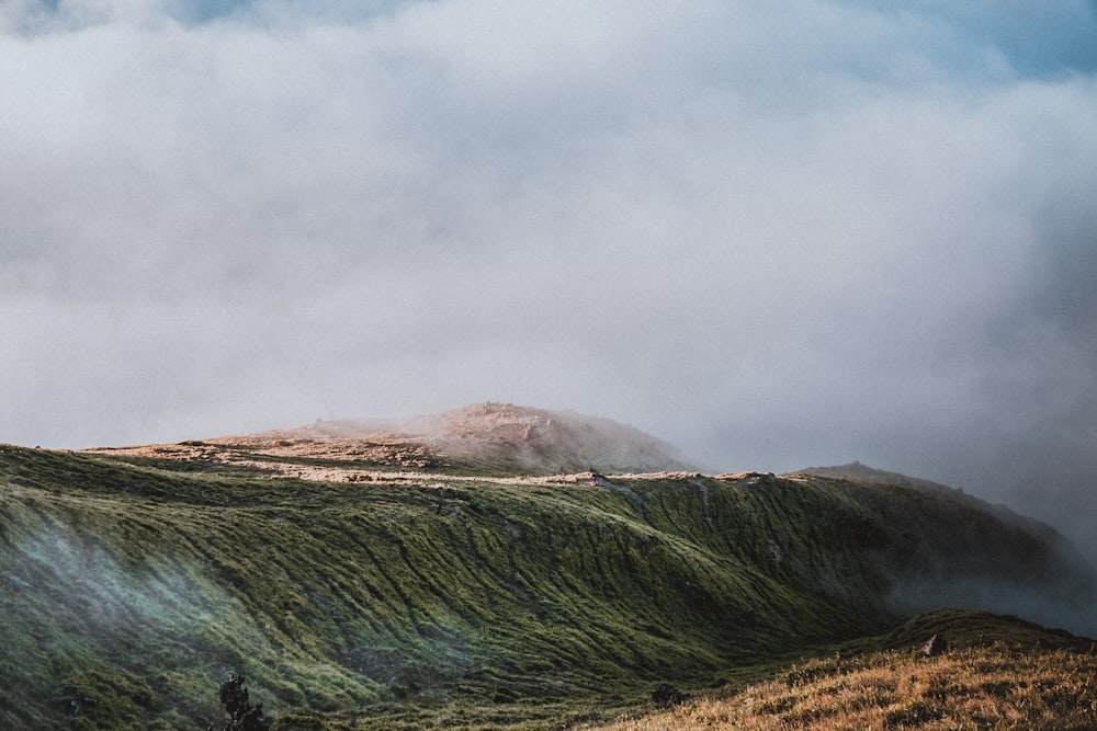 mountain with green grass under white clouds and blue sky