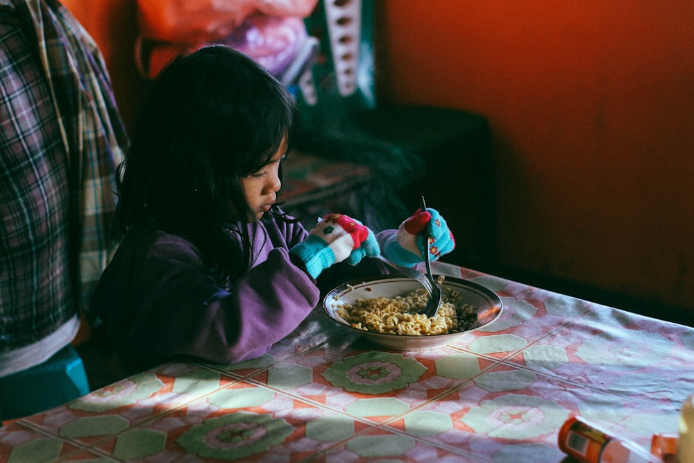 menina segurando colher enquanto come macarrão
