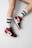 A pair of legs wearing high-top sneakers in red, black, and white colors paired with white socks that have 'Vetements' written in red. The socks also have black stripes near the top.