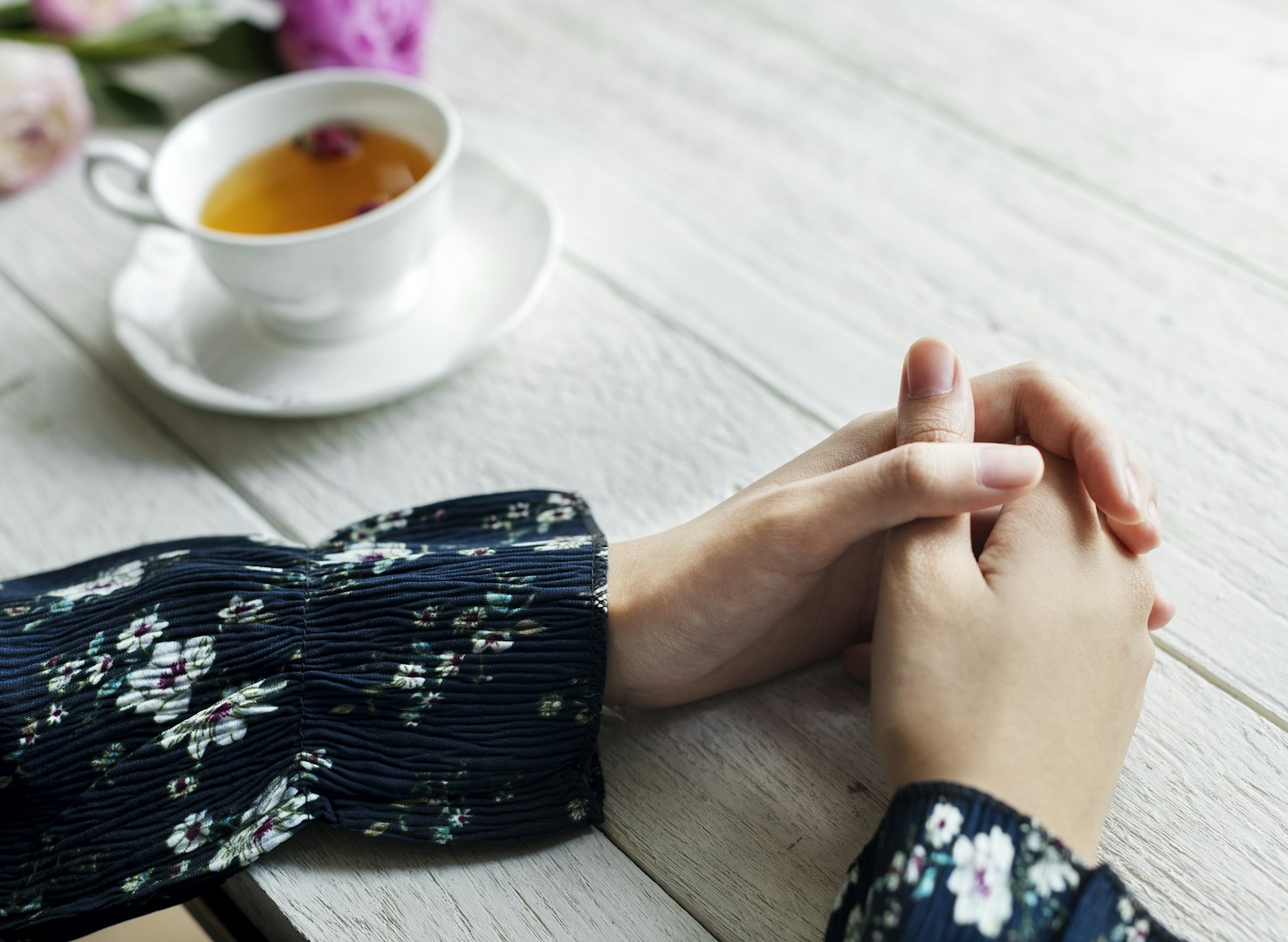 woman sitting at a table with clasped hands and a cup of tea