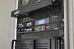 A server rack containing various network and power management devices. The devices feature buttons, switches, and digital displays, indicating active usage and monitoring capabilities. The rack has a black metal mesh design for ventilation.
