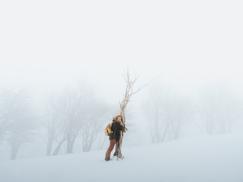 person hugging bare tree while snow
