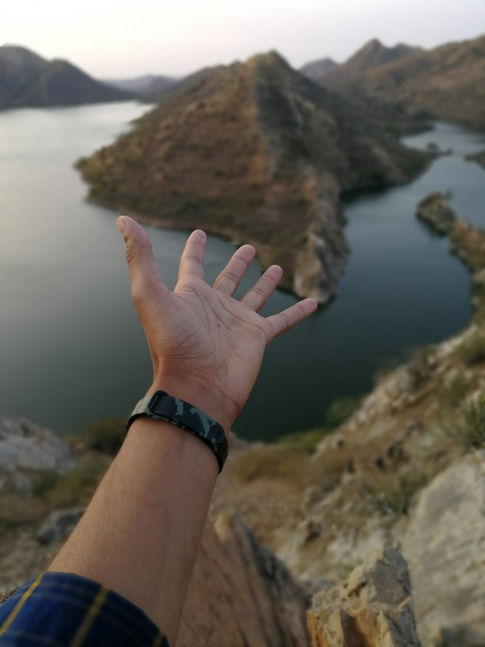person's hand pointing to body of water and hill