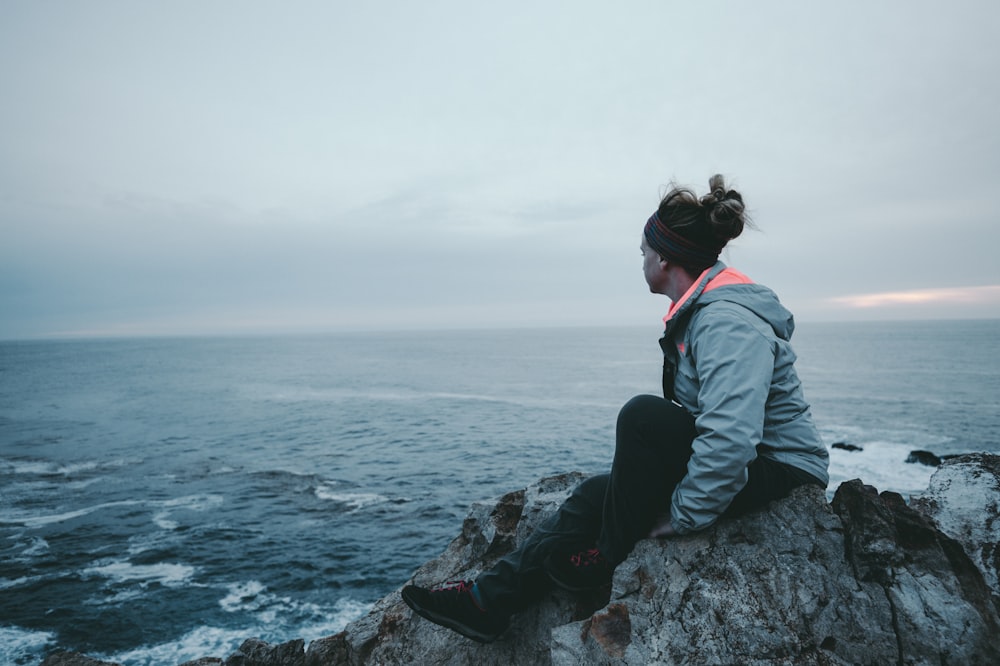 woman sitting on cliff near sea