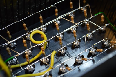 A close-up view of an electronic circuit board featuring several resistors, wires, and connections. Yellow and green wires loop through a grid of small components held together by metal frameworks.