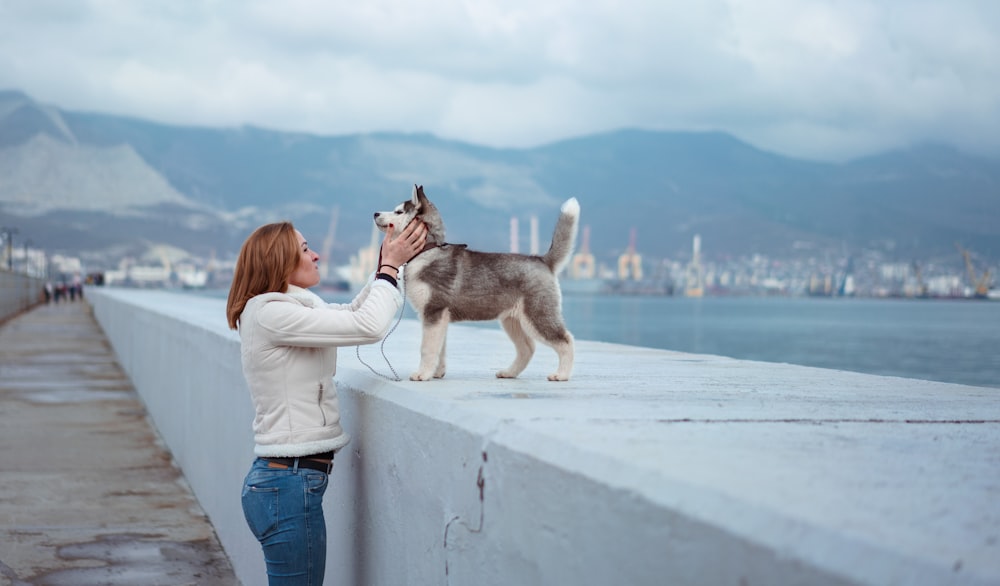 Frau, die steht, während sie einen Syberian Husky-Welpen in der Nähe des Meeres hält