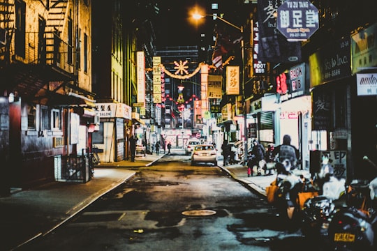 cars and motorcycles on road in between buildings in Chinatown United States