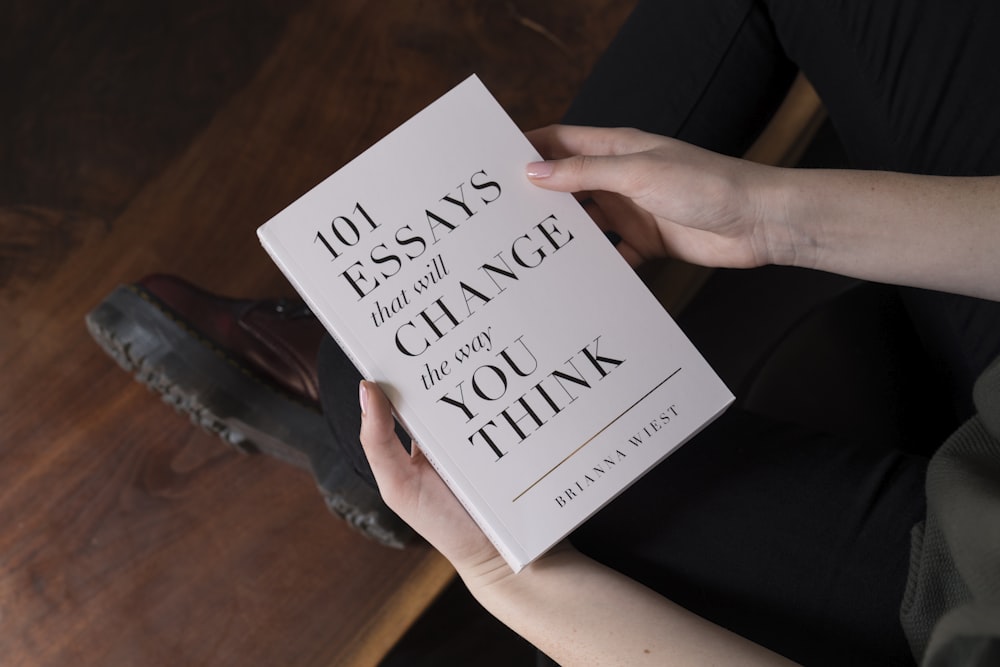person holding 101 Essay that will Change the way you Think book