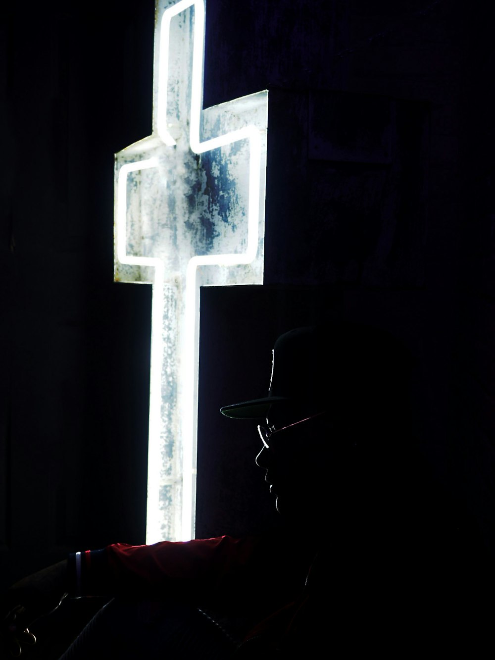 흰색 십자가 네온 간판 근처에 앉아있는 사람
