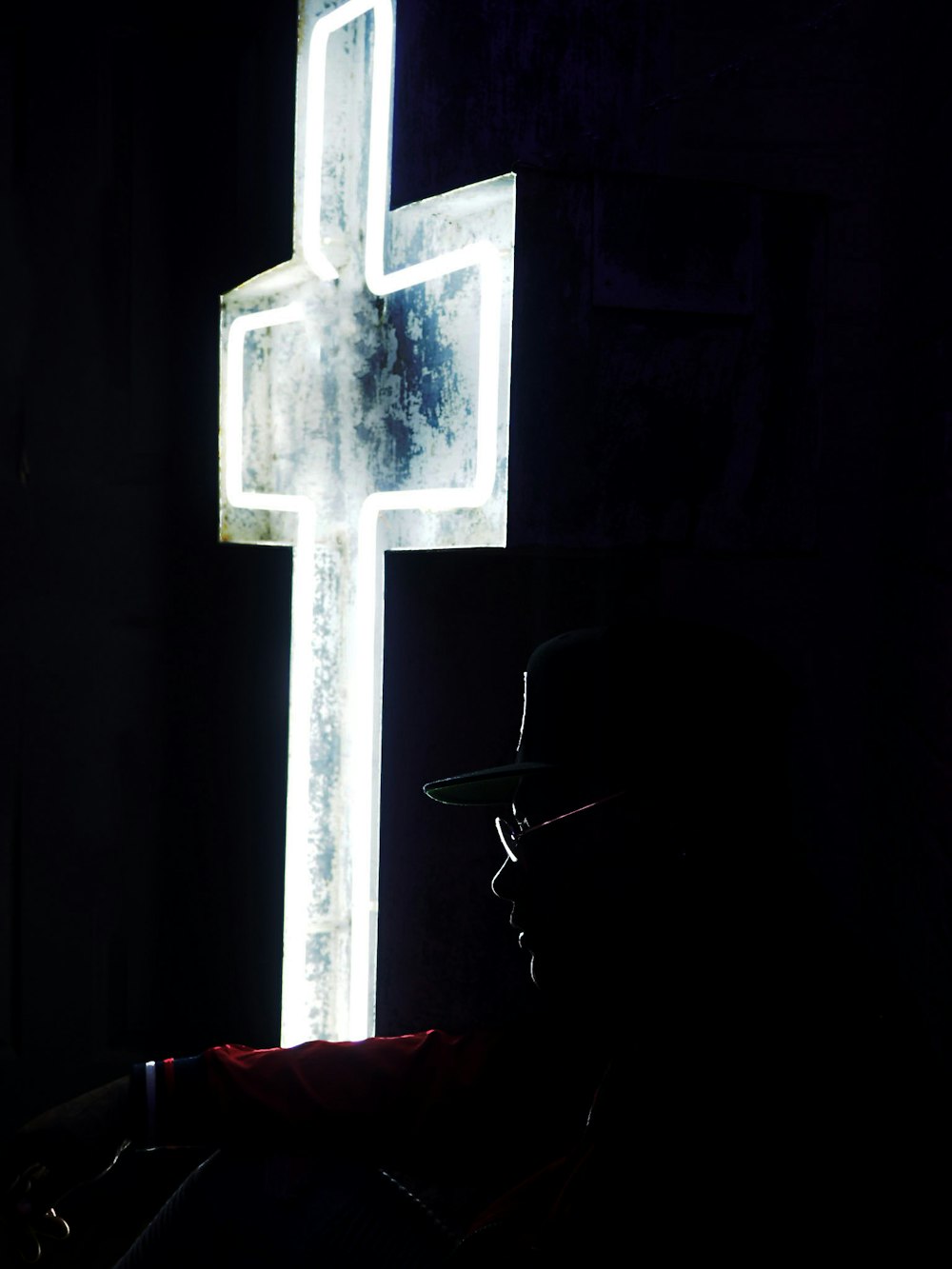 person sitting near white cross neon signage