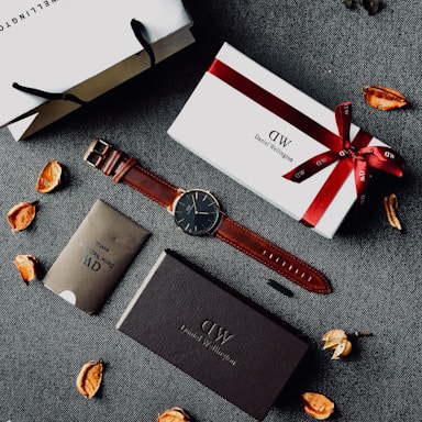 round black analog watch with brown leather stral with box and paper tote bag on gray yextile