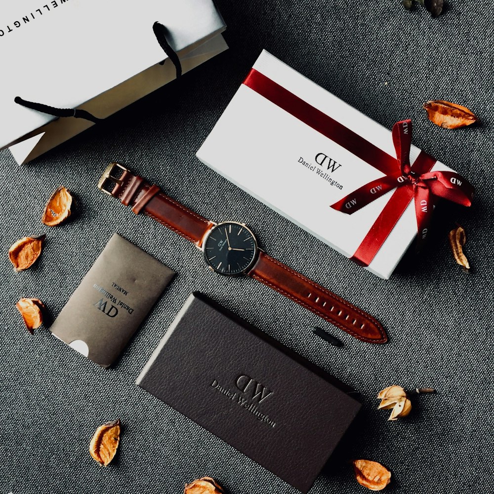 round black analog watch with brown leather stral with box and paper tote bag on gray yextile
