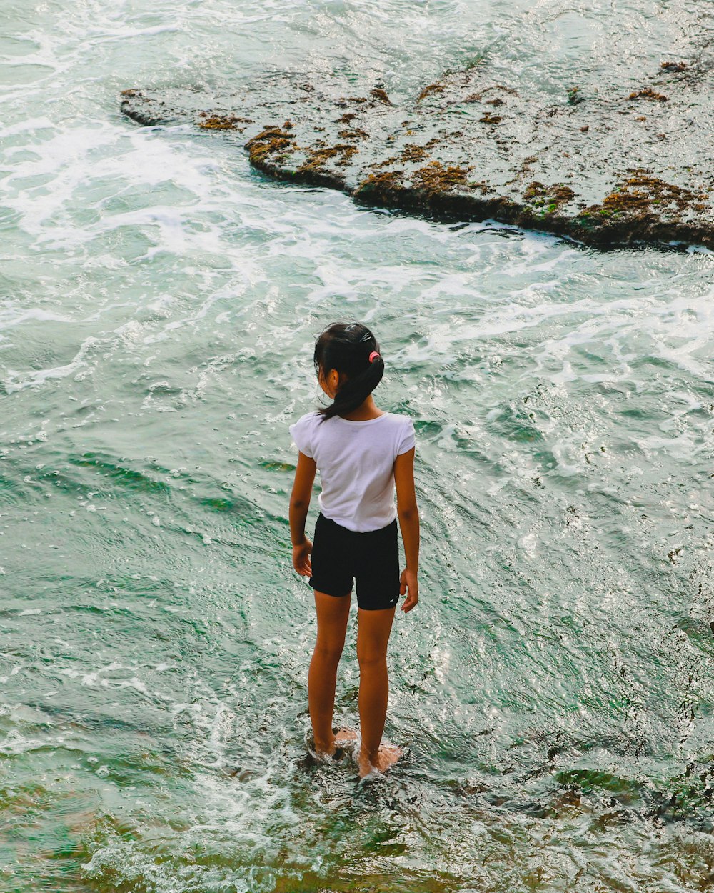 girl standing on the rock and body of water