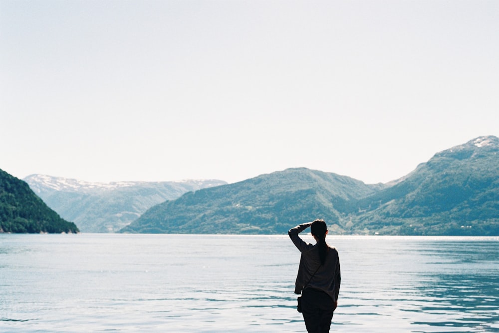 Silhouette d’une personne près d’un plan d’eau et de montagnes pendant la journée