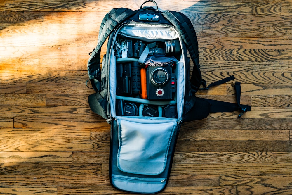 Flat-Lay-Fotografie einer DSLR-Kamera im Rucksack auf Holzparkettboden