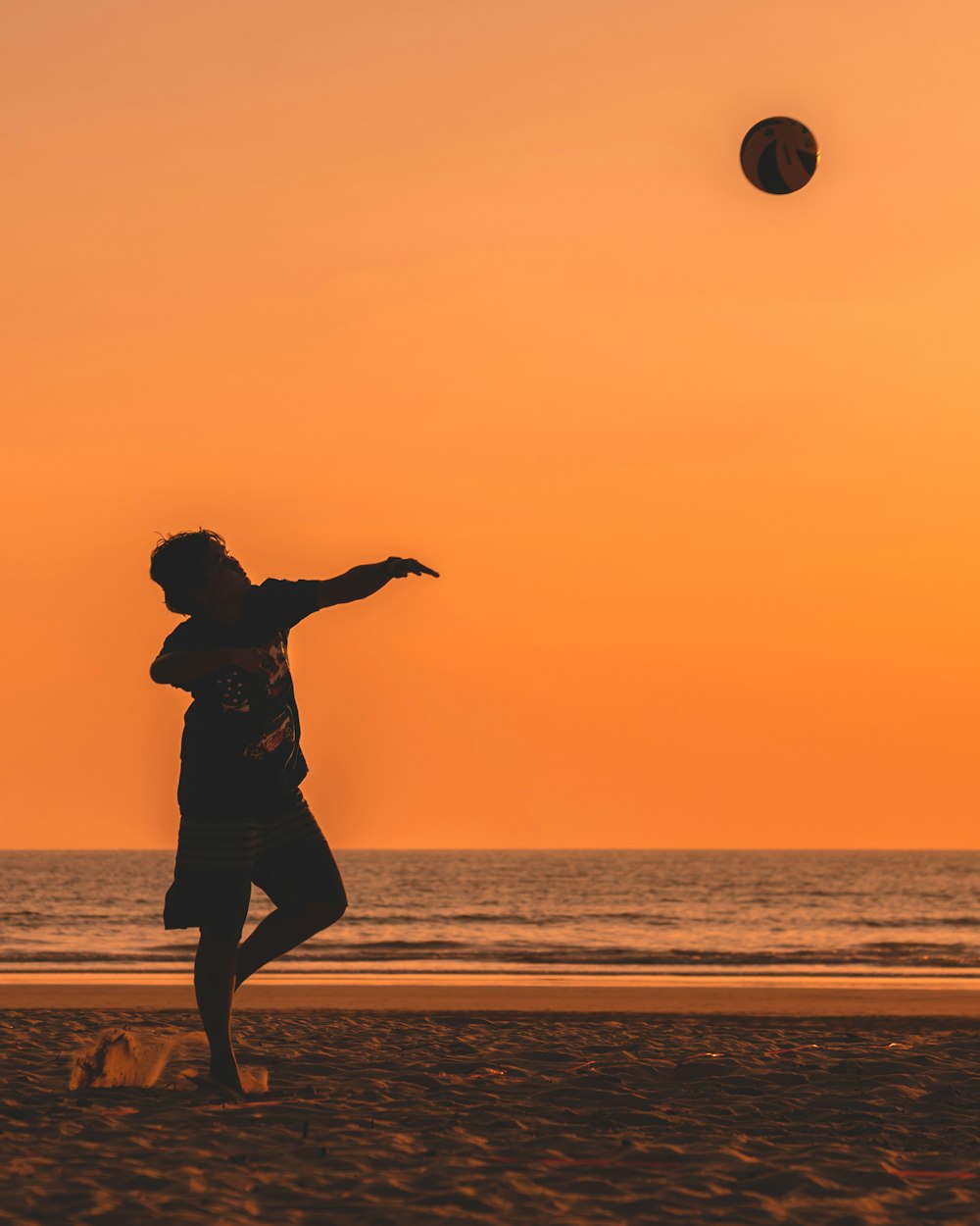 Silhouette eines Mannes, der zur goldenen Stunde einen Ball in der Nähe des Ozeans wirft