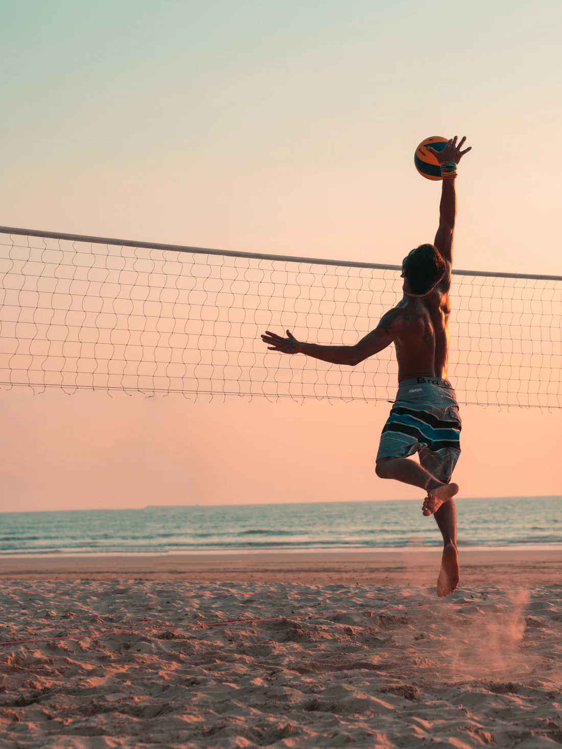 A beach volleyball player jumping to hit the ball over the net