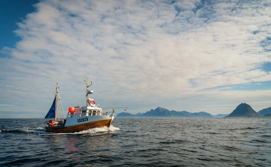 A sturdy fishing boat cutting through calm ocean waters under a clear sky.