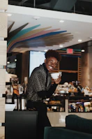 A smiling person holding a cup of coffee in a cozy café.