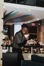 A barista happily serving coffee in a cup made by Cafecup inside a cozy cafe.
