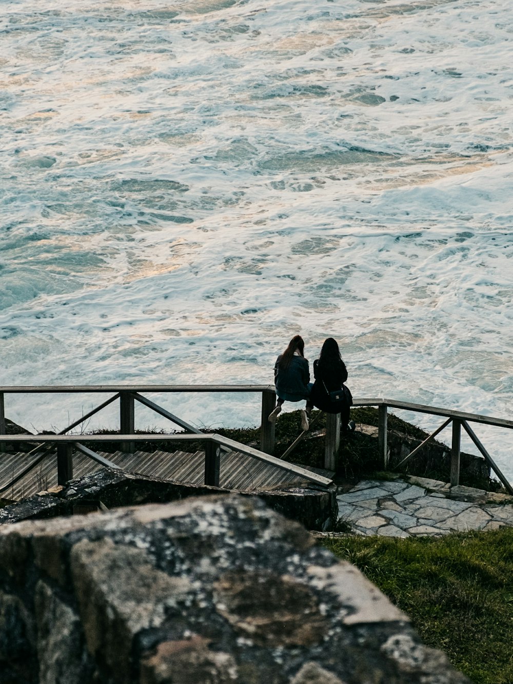 two woman sitting on bridge baluster