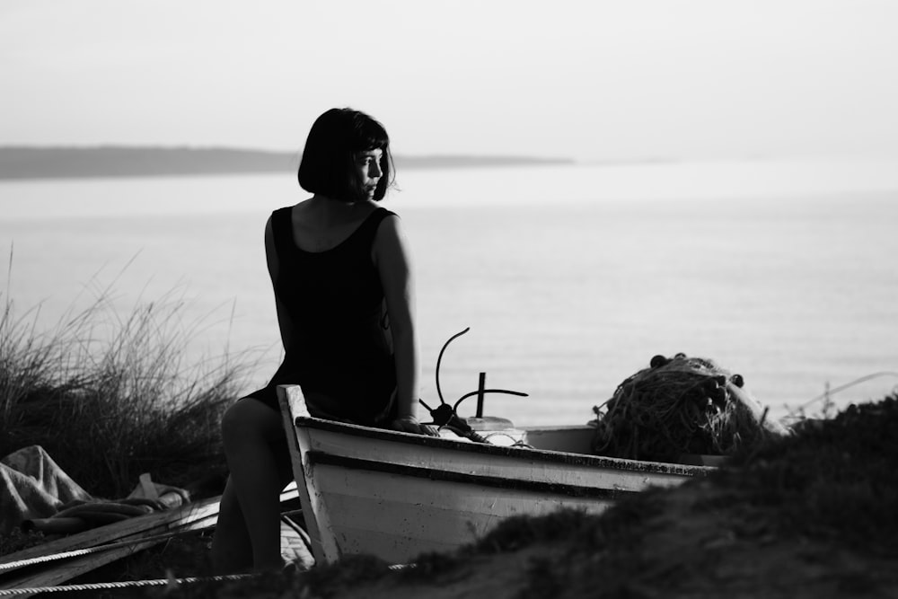 grayscale photo of woman sitting on boat while looking at the sea