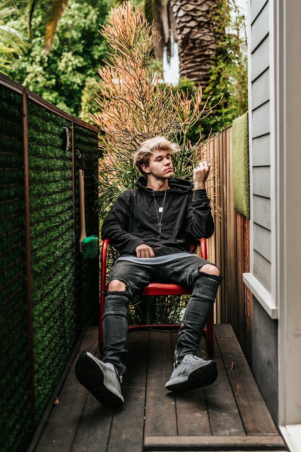 man sitting on red metal armchair near green grass framed divider