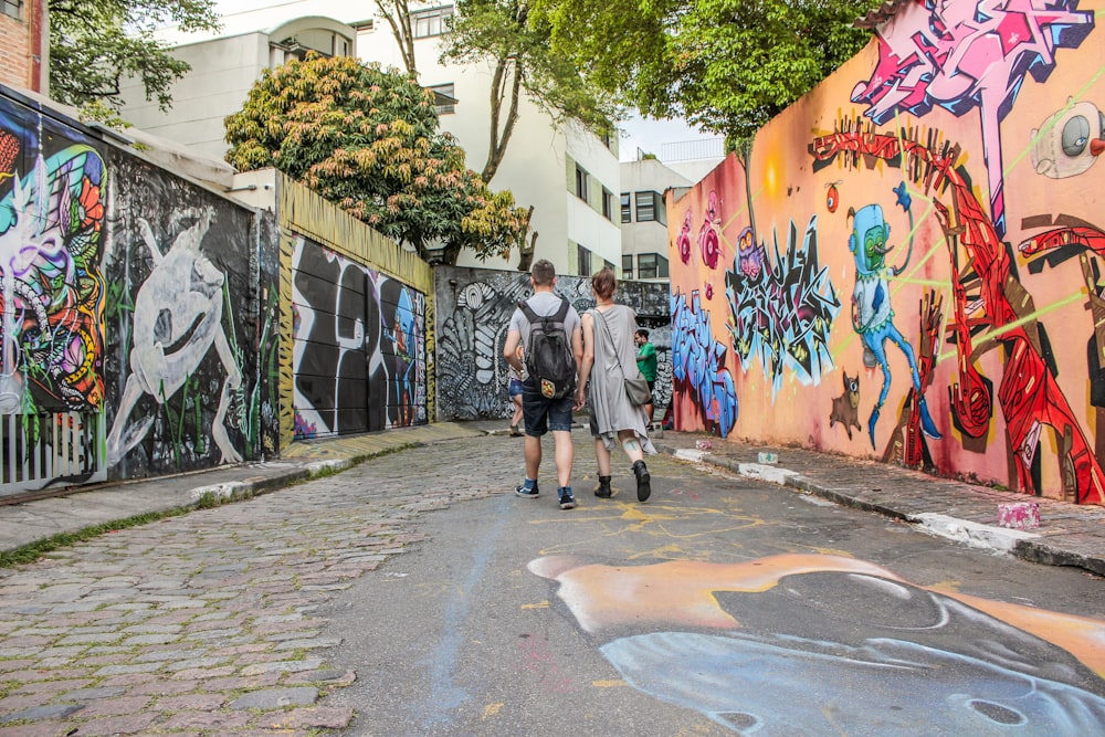 man and woman standing between wall with graffiti artwork