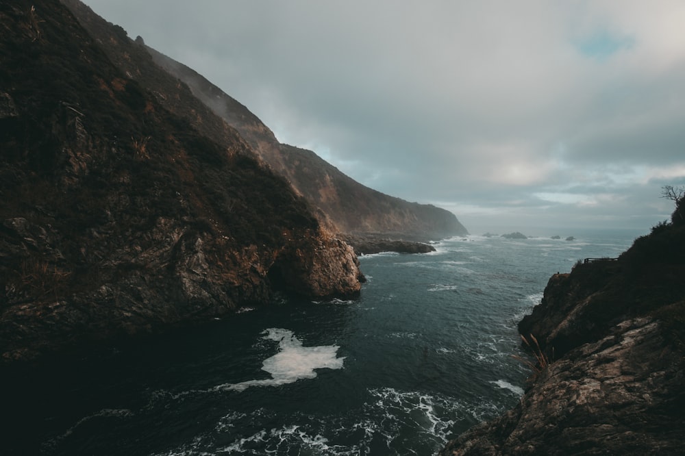 body of water between mountain under cloud