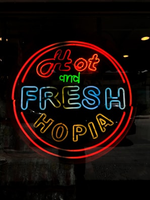 A neon sign displays the words 'Hot and Fresh Hopia' in bright, colorful letters. The sign features a vibrant red border with 'Hot' in red, 'and' in green, 'Fresh' in blue, and 'Hopia' in yellow letters.