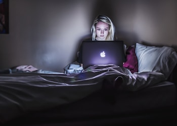 woman sitting on bed with MacBook on lap