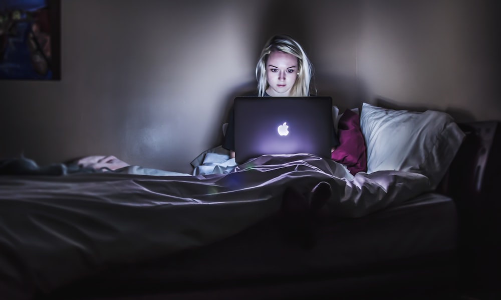 woman sitting on bed with MacBook on lap looking at sites on the dark web selling her data