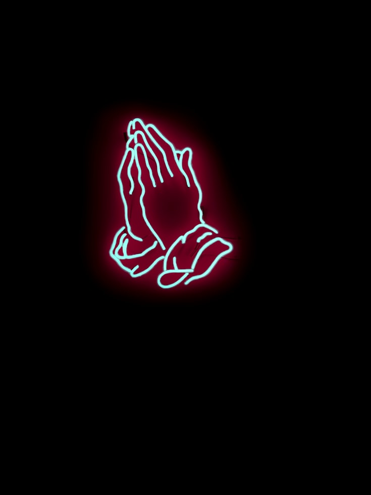 Neon prayer hands on a black background.