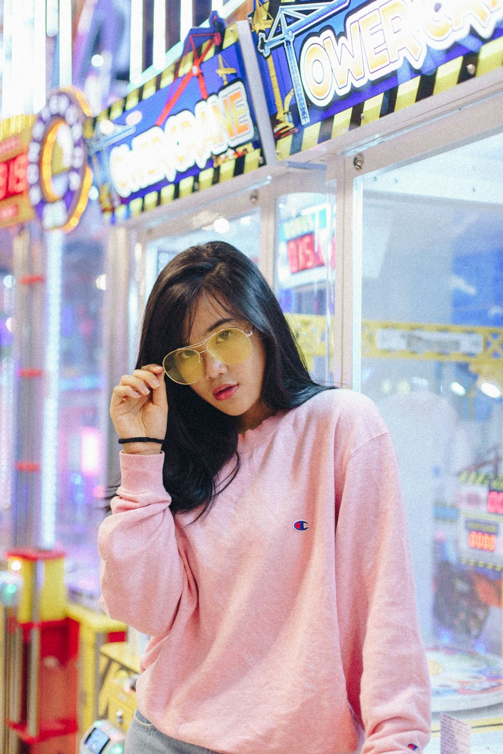 woman in pink Champion sweatshirt holding her sunglasses leaning on game machine