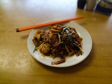 A sizzling plate of Chinese noodles and fast food items on a wooden table.