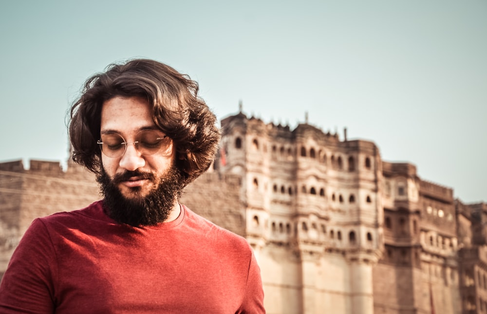 Homem vestindo camisa vermelha de gola alta perto do antigo palácio