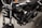 A close-up view of a black motorcycle, focusing on the engine and components. The chrome and metallic parts are polished, with the brand name prominently displayed on the side. The background appears to be a dark, textured surface.