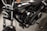 A close-up view of a black motorcycle, focusing on the engine and components. The chrome and metallic parts are polished, with the brand name prominently displayed on the side. The background appears to be a dark, textured surface.