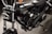 A close-up view of a black motorcycle, focusing on the engine and components. The chrome and metallic parts are polished, with the brand name prominently displayed on the side. The background appears to be a dark, textured surface.